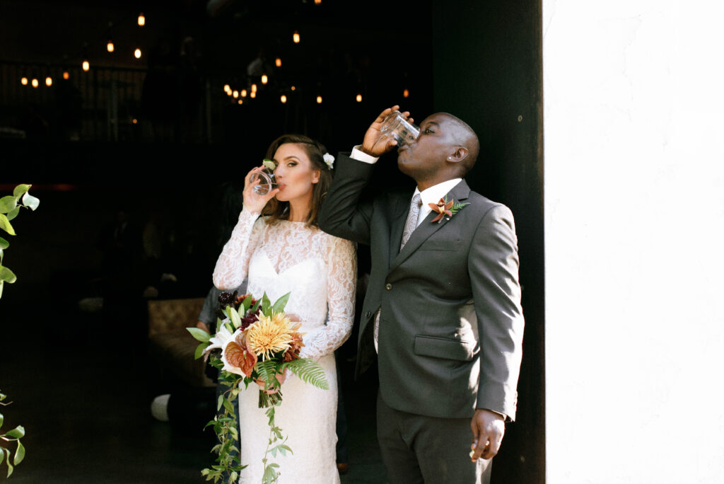 Edited wedding photo with true-to-life tones showing bride and groom taking a shot together after ceremony