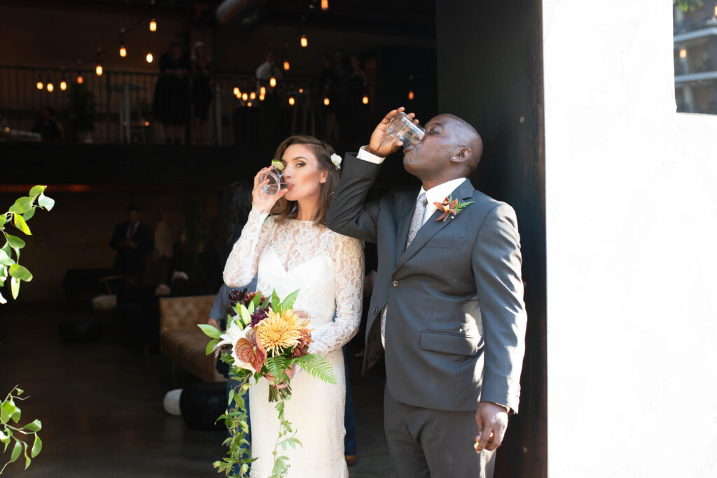Unedited wedding photo of bride and groom taking a celebratory shot together outside their venue