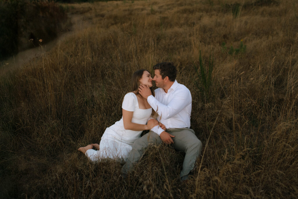 Couple sitting in tall grass during a Discovery Park engagement session in Seattle Washington
